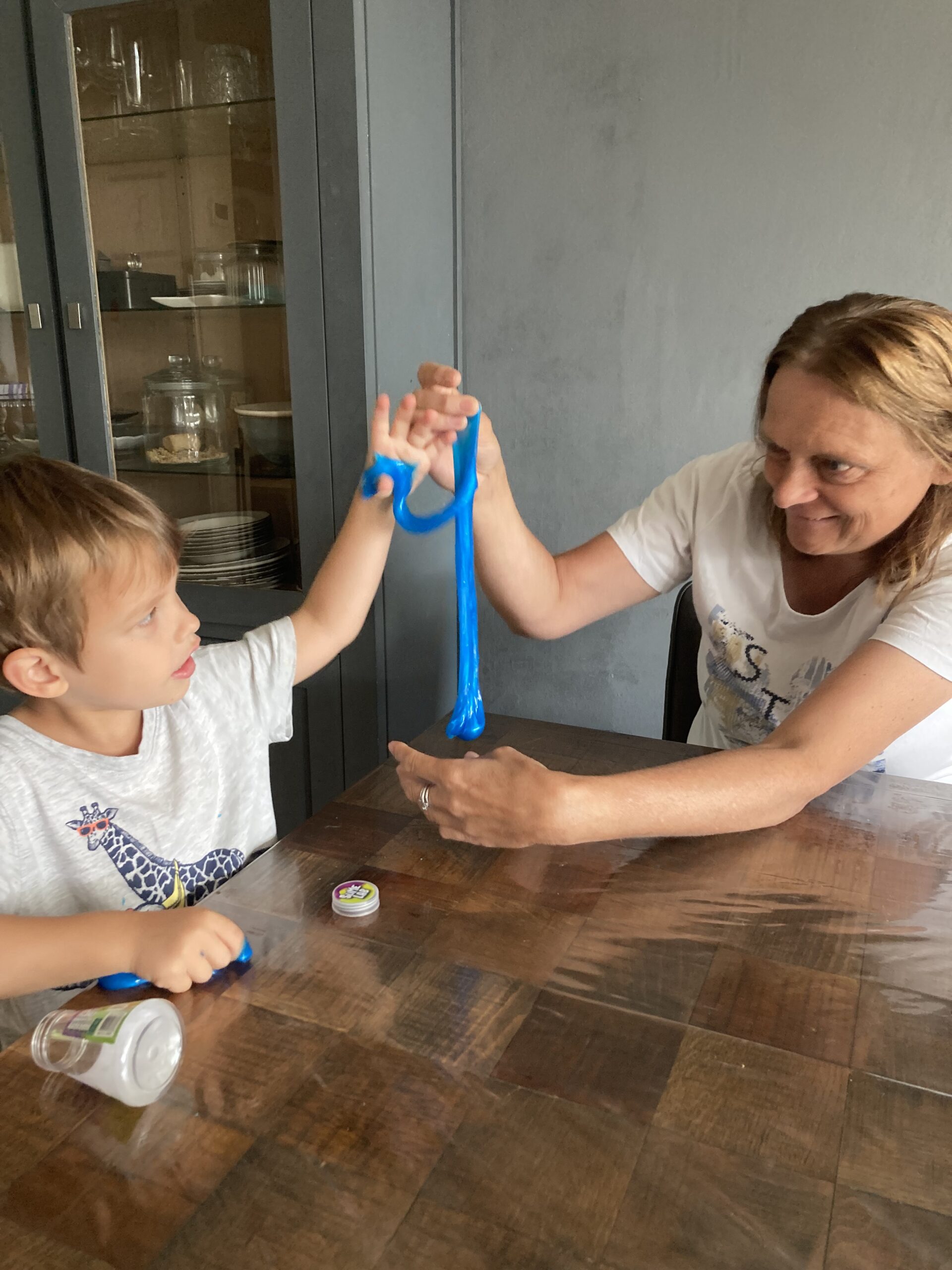 Coach en kind zitten aan tafel hebben blauw slijm vast wat naar beneden loopt. Het kind krijgt begeleiding voor autisme